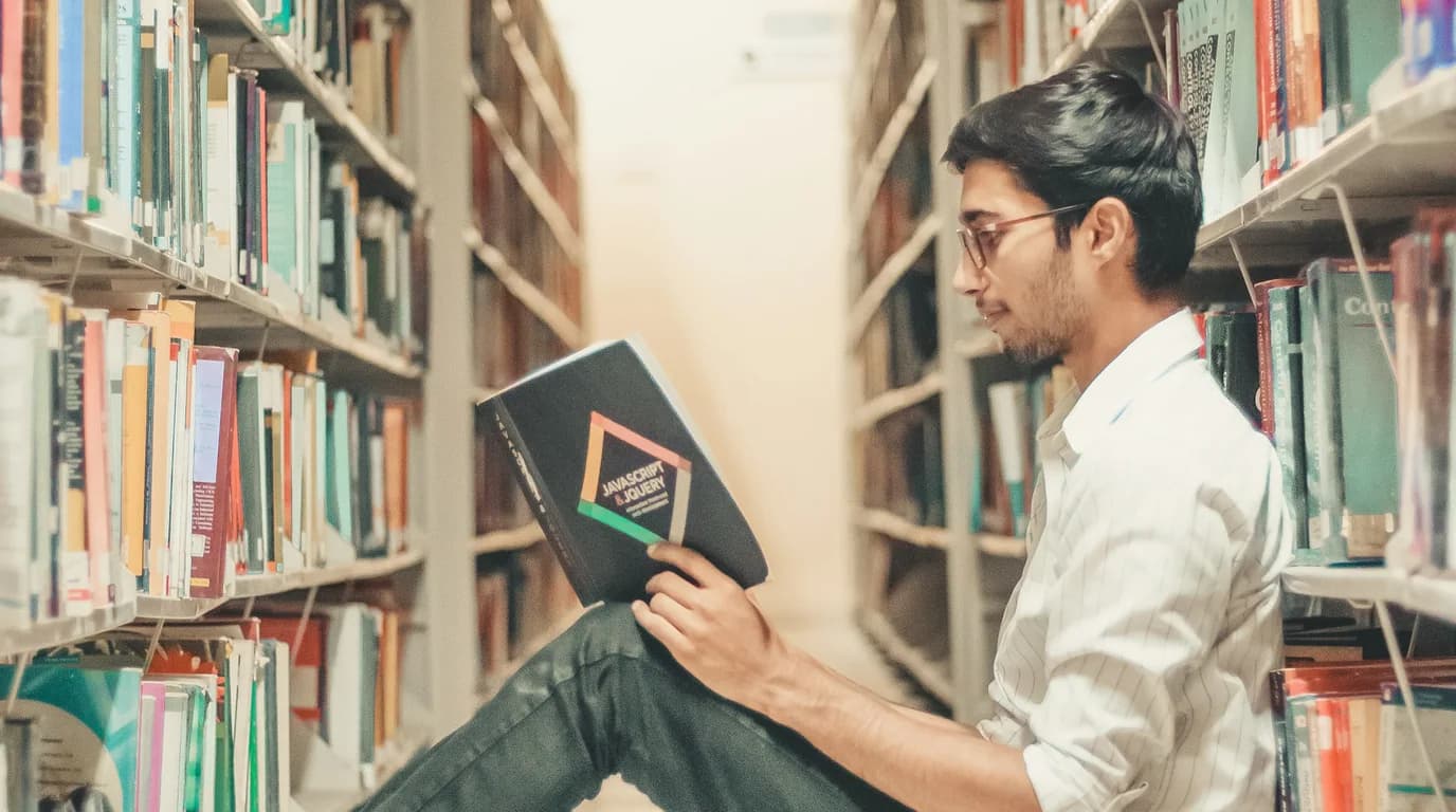 A student reading a book between library shelves