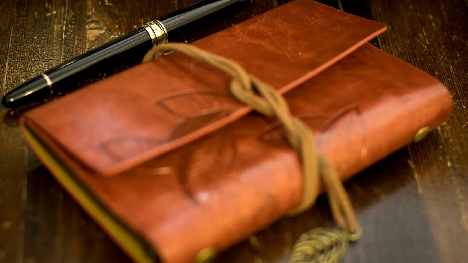 A fountain pen resting on a brown leather notebook on a wooden table