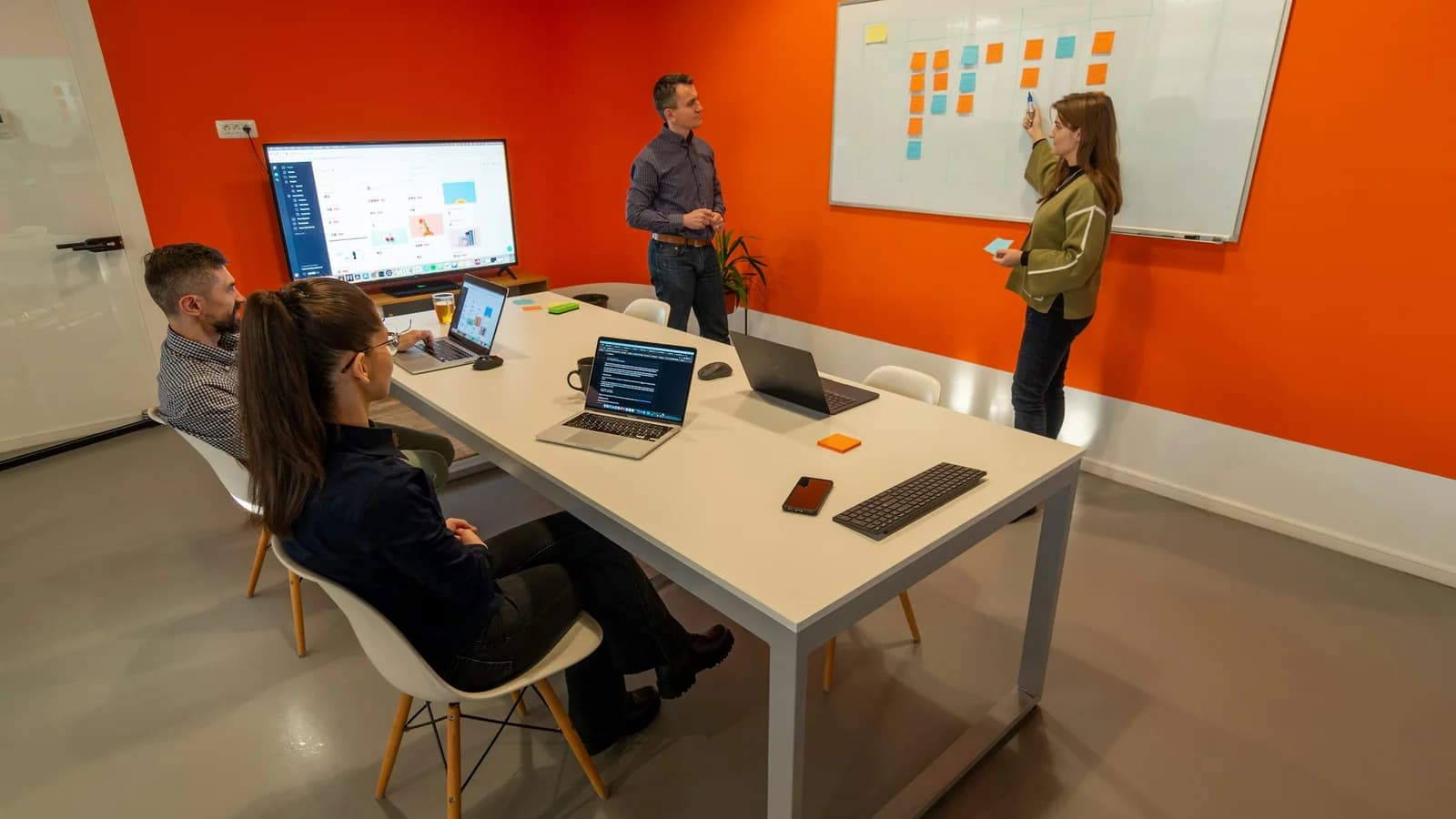 Colleagues planning work with laptops and a whiteboard in an orange meeting room